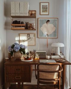 a wooden desk topped with a laptop computer next to a lamp and pictures on the wall