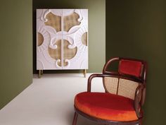 a red chair sitting in front of a white wall with an art piece behind it