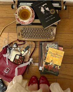 a woman's feet are on the floor next to books and a typewriter