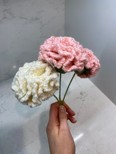 a person holding three crocheted flowers in their hand on a marble countertop