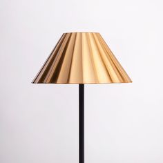 a gold lamp on a black stand against a white wall with a clock above it