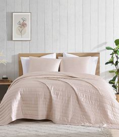 a bed with pink comforter and pillows in a room next to a potted plant