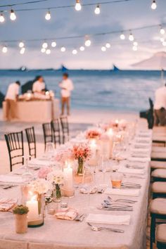 a long table is set up with candles and place settings for an outdoor dinner on the beach