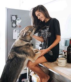 a woman sitting at a kitchen counter petting a dog's head with its mouth open