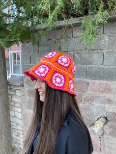 a woman standing next to a brick wall wearing a red and pink knitted hat