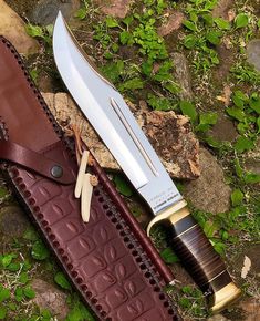 a knife and sheath laying next to each other on the ground with green plants in the background