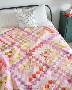 a bed with a pink and yellow quilt on it's headboard next to a night stand