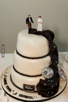 a wedding cake with two figurines on top and black ribbon around the base