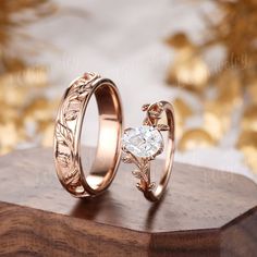 two gold wedding rings sitting on top of a wooden stand with flowers and leaves in the middle