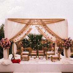 an outdoor wedding setup with white drapes and pink flowers on the table, along with gold chairs