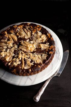 a chocolate cake topped with nuts on top of a white plate next to a knife