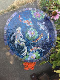 there is a blue plate with fish on it in the ground next to some flowers