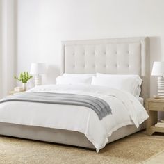 a bed with white linens and pillows in a clean bedroom area next to two nightstands