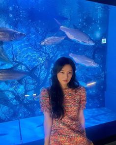 a woman standing in front of an aquarium with fish on the wall and water behind her