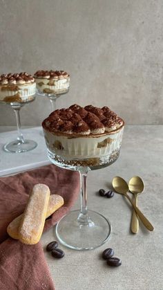 two desserts sitting on top of a table next to spoons and utensils