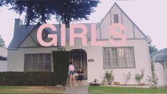 two women standing in front of a house with the word girls painted on it