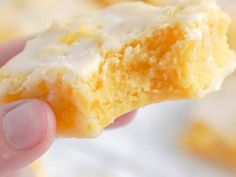 a hand holding a piece of cake with icing on it's side and the rest of the pastry in the background