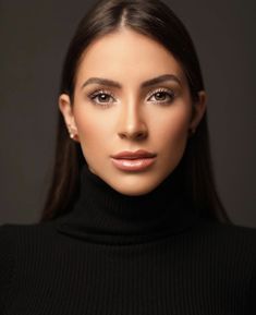 a woman with long dark hair wearing a black turtle neck sweater and gold hoop earrings