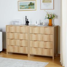 a wooden dresser sitting next to a white chair in a room with pictures on the wall