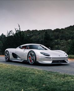 a silver sports car driving down a road next to some green grass and trees in the background