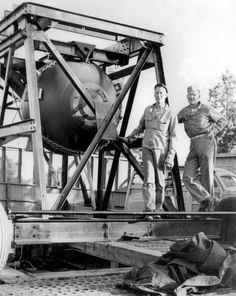 two men standing next to each other near a large object on a truck bed that is being unloaded
