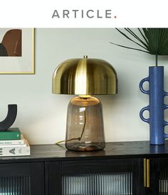 a table lamp sitting on top of a wooden cabinet next to a vase and books