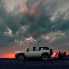 a white truck parked on top of a sandy beach under a cloudy sky with tents