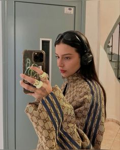 a woman wearing headphones taking a selfie in front of a mirror with her cell phone