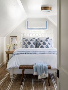 a white bed with blue and white comforter in a small attic bedroom on top of a carpeted floor