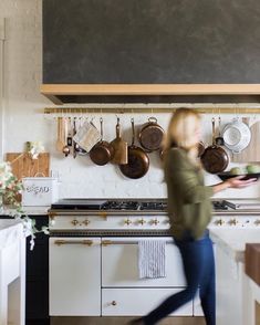 a woman is running in the kitchen with pots and pans hanging on the wall