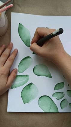 a person is drawing leaves on paper with a black pen while another hand holds a pencil