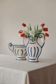two white and blue vases with flowers in them sitting on a tableclothed surface
