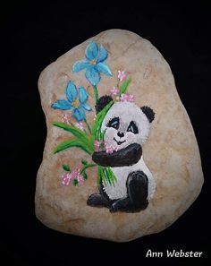a rock with a painting of a panda bear holding flowers on it's side
