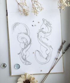 some flowers are sitting on top of a piece of paper and next to it is a drawing of two mermaids