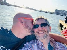 two men are sitting on a boat in the water and one is kissing the other