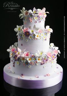 a three tiered white cake with flowers on it's side and the words happy birthday written below