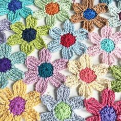 crocheted flowers are arranged in rows on a white tablecloth with multicolored yarns