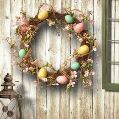 an easter wreath on a wooden wall with flowers and eggs painted on it, next to a lantern