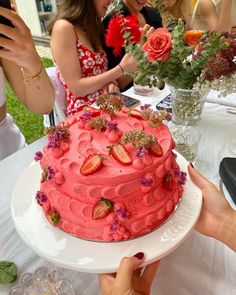 a group of women standing around a table with a cake on it and flowers in the middle