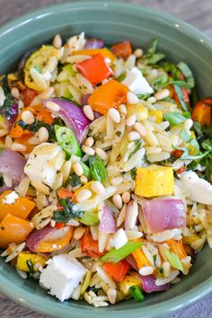 a green bowl filled with rice, vegetables and other things on top of a wooden table