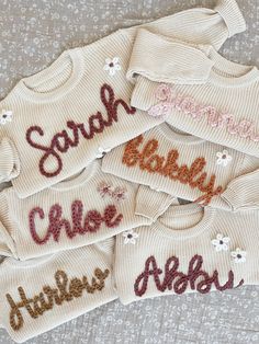 several sweaters with names on them sitting on a bed