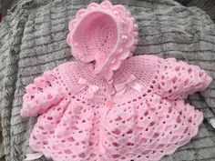 a pink crocheted sweater and hat sitting on top of a gray knitted blanket