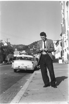 a man standing on the side of a road next to a car and looking at his cell phone