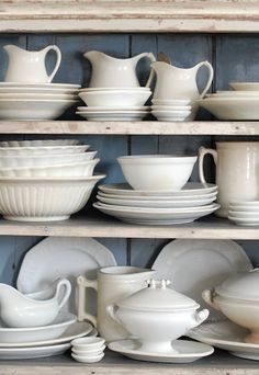 white dishes are stacked on top of each other in a shelf with wooden shelves behind them