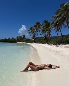 a woman laying on the beach with palm trees in the backgroung and clear blue water
