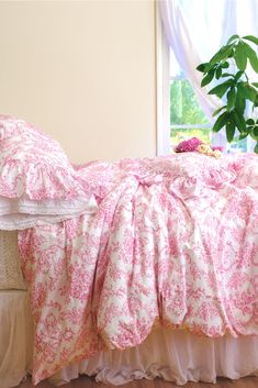 a bed with pink and white comforters on top of it next to a potted plant