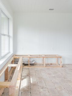 an empty room with white walls and wooden benches on the floor in front of a window