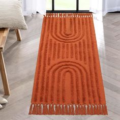 an orange rug with fringes on the floor in front of a chair and window