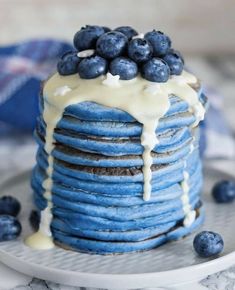 a stack of blueberry pancakes with icing drizzled on top and topped with fresh blueberries