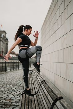a woman in black top and grey leggings doing yoga on bench next to wall